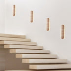 Four Clérachic wall lights stepping up a white wall above a staircase of pale floating treads.