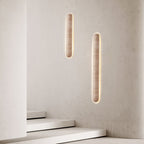 Pair of lit Clérachic travertine sconces on a textured light wall, with white stairs at the foot of the frame.