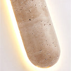 Close view of the rounded end of this Clérachic wall light, showing the pitted travertine surface and warm light behind.