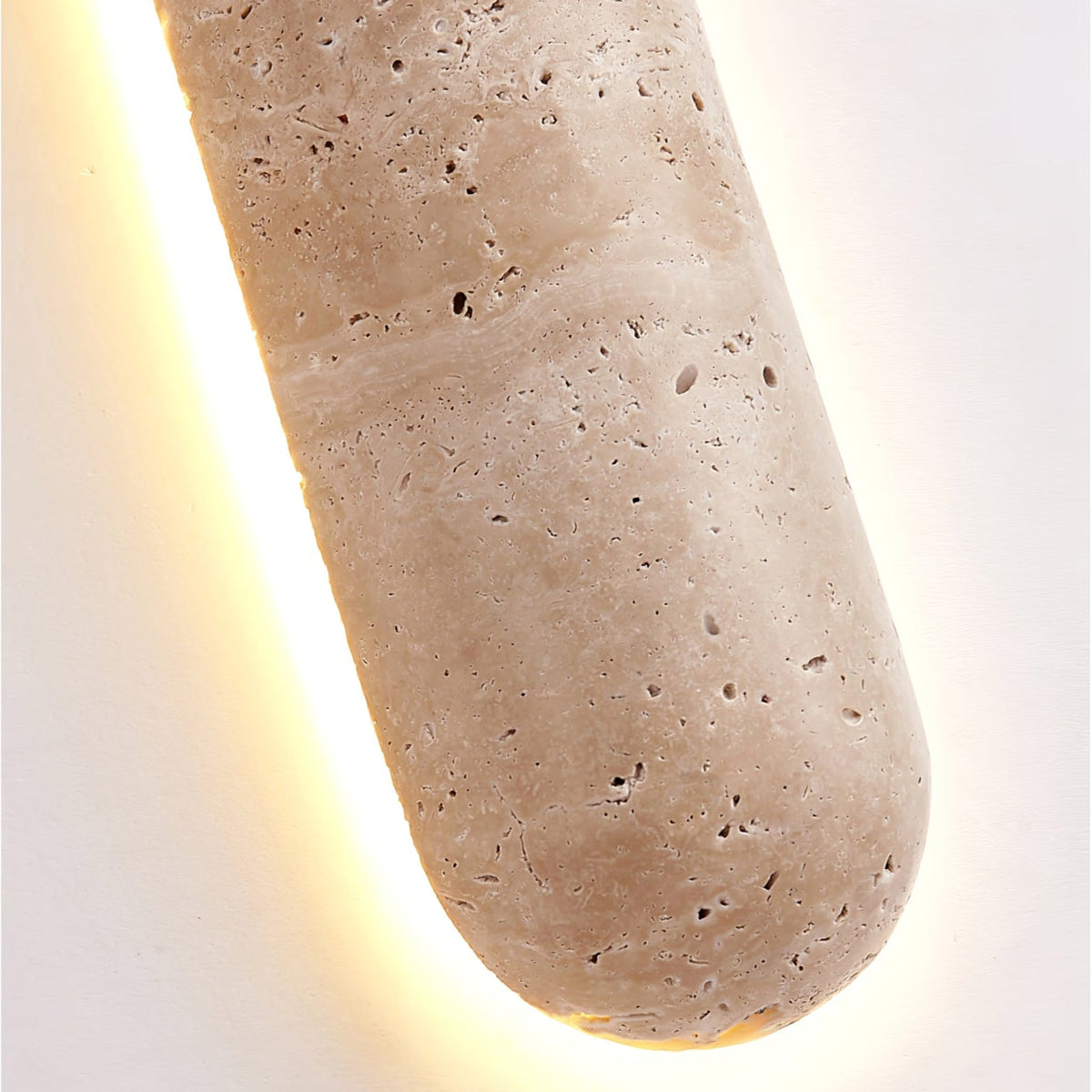Close view of the rounded end of this Clérachic wall light, showing the pitted travertine surface and warm light behind.