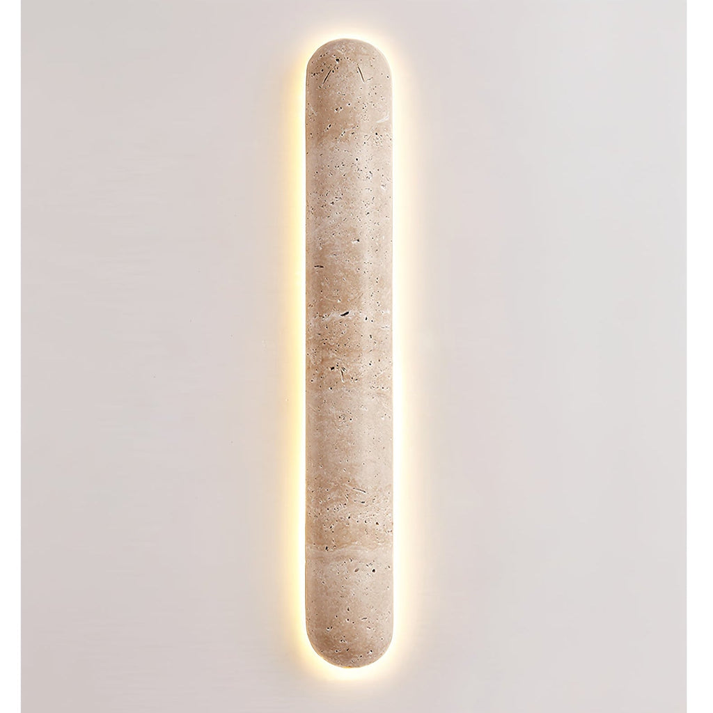 Lit Clérachic travertine wall light with a bright warm halo around its edge, on a plain light wall.