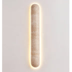 Lit Clérachic travertine wall light with a bright warm halo around its edge, on a plain light wall.
