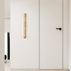 Small Clérachic wall light glowing on a white wall beside a flush door with a black handle.