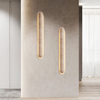 Two Clérachic wall lights of different lengths on a stone-grey column, with sheer curtains and a pale floor beyond.