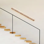 Angled Clérachic wall light above a glass stair rail, with wooden steps rising beneath it.