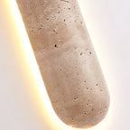 Detail of the travertine end of this Clérachic wall light, its natural holes and pale bands lit from behind by a warm glow.