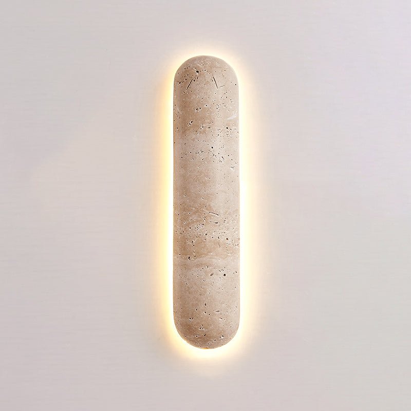 Short Clérachic wall light on a soft pink-grey wall, its banded travertine body ringed by a warm glow.