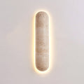 Short Clérachic wall light on a soft pink-grey wall, its banded travertine body ringed by a warm glow.