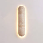 Short Clérachic wall light on a soft pink-grey wall, its banded travertine body ringed by a warm glow.