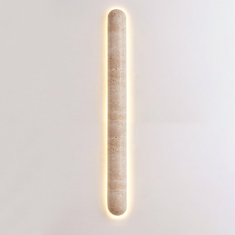Very long, narrow Clérachic travertine wall light lit on a pale wall, with a thin glow along each side.