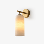 Clérachic Pillar wall light lit on white, warm glow rising through the veined alabaster shade.