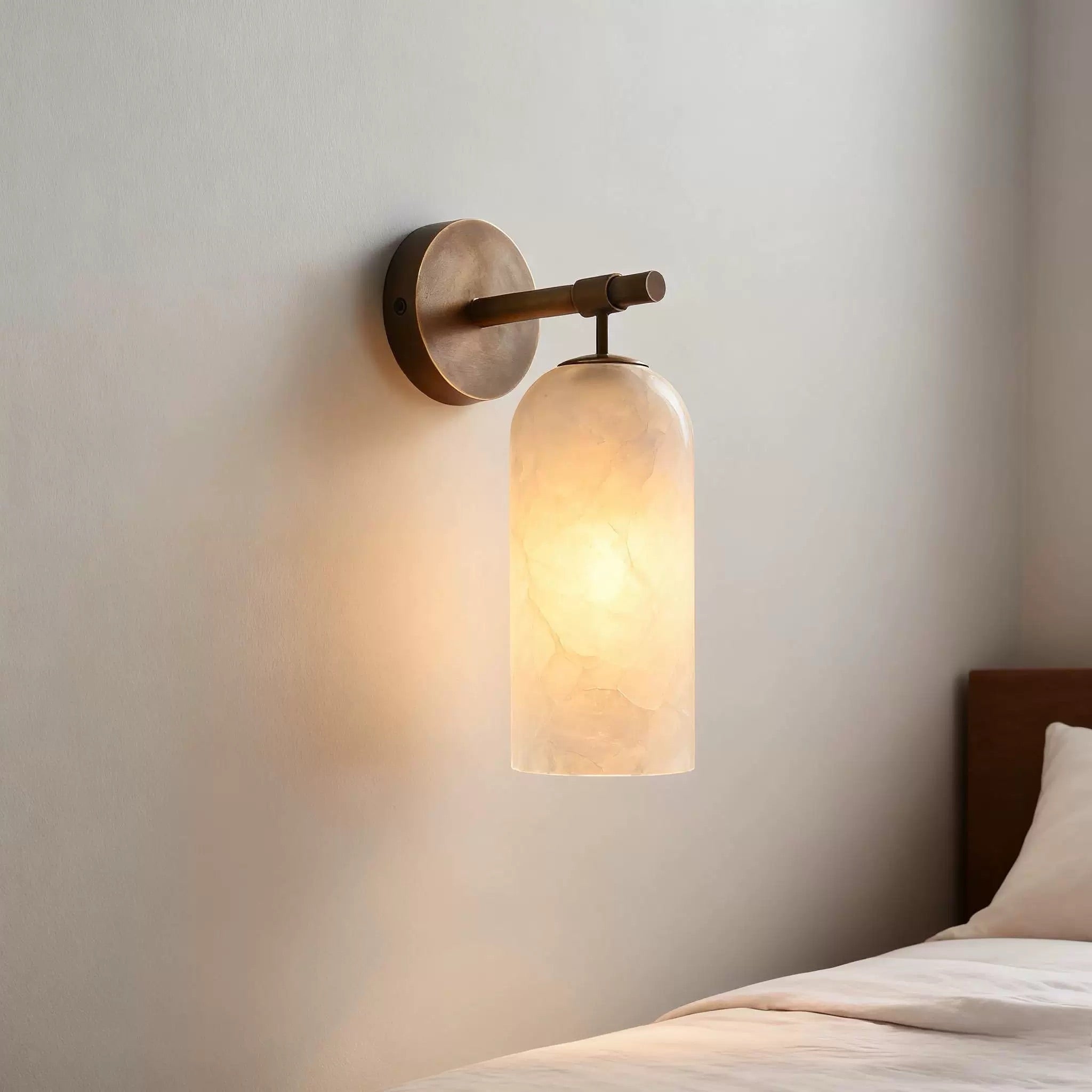Clérachic Pillar wall light glowing beside a bed, soft light pooling across the plaster.