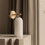 The Clérachic Pillar wall light on a stone block, brass disc and arm catching the daylight.