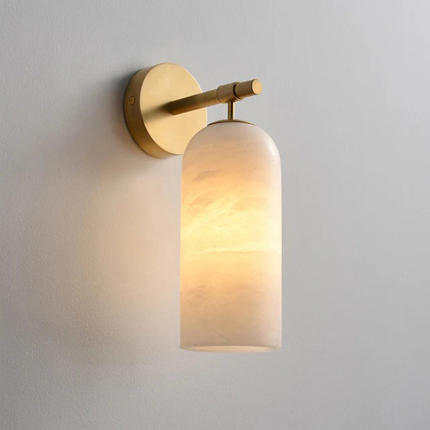 Clérachic Pillar wall light lit close on a pale wall, warm light held inside the stone dome.