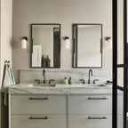 Clérachic Pillar wall lights flanking two black-framed mirrors above a marble double vanity.