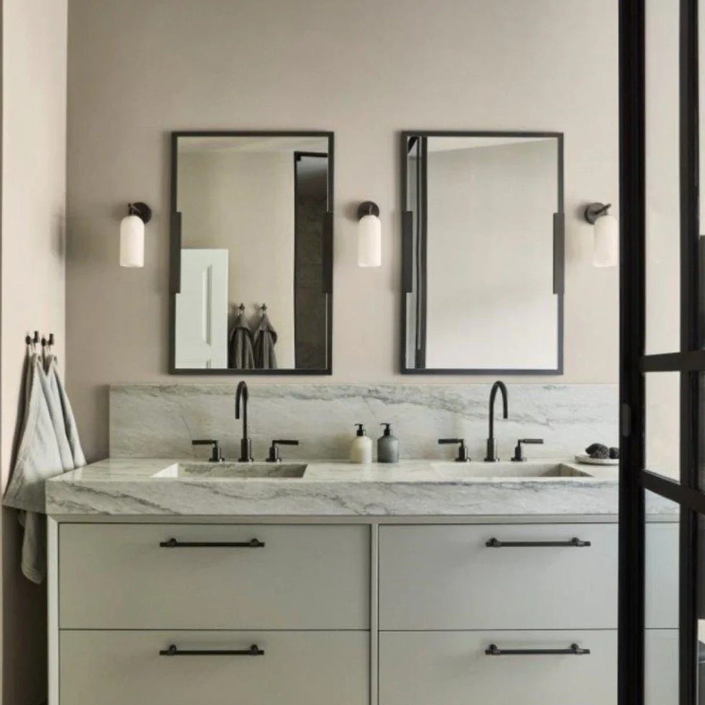 Clérachic Pillar wall lights flanking two black-framed mirrors above a marble double vanity.