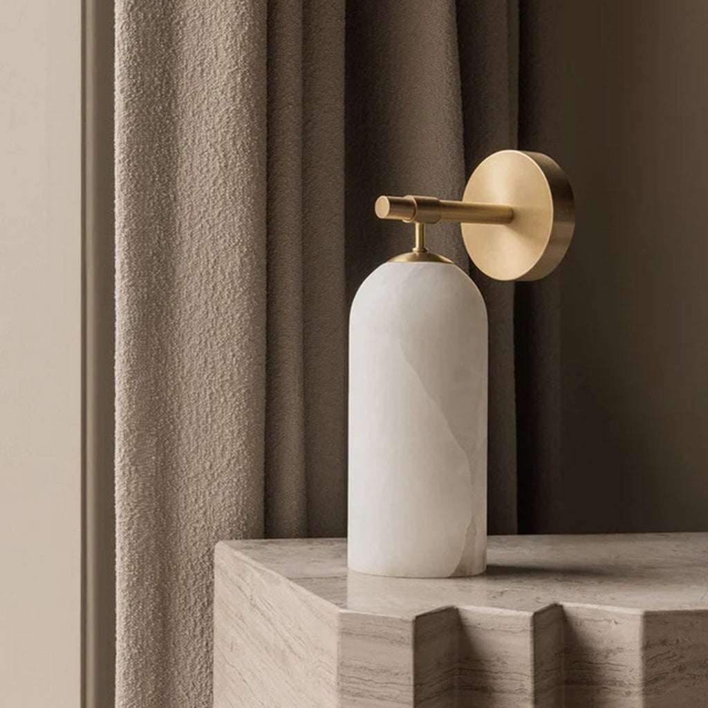 The Clérachic Pillar wall light angled on travertine, showing its rounded alabaster underside.