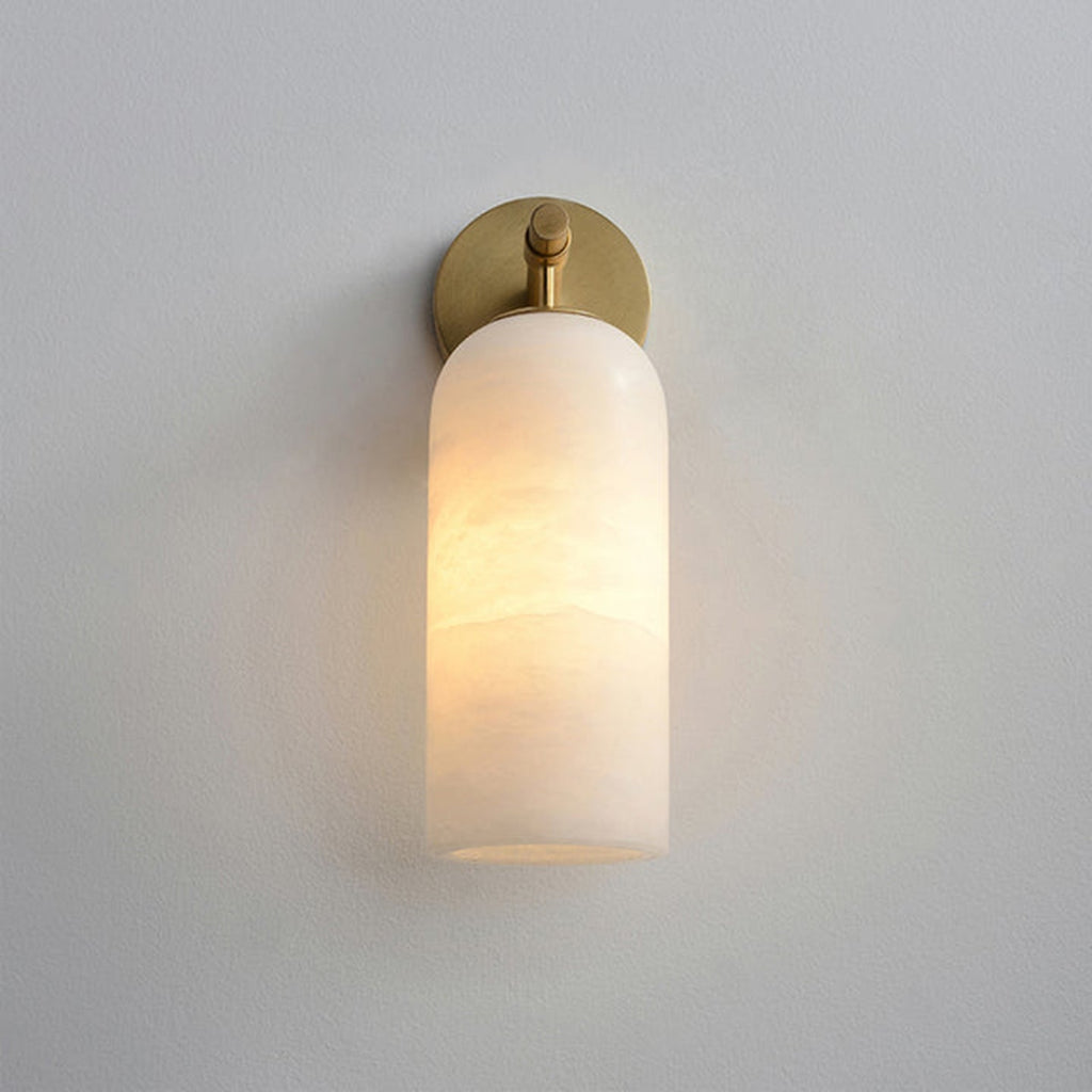 Clérachic Pillar wall light lit on grey, slim brass stem dropping to the glowing shade.