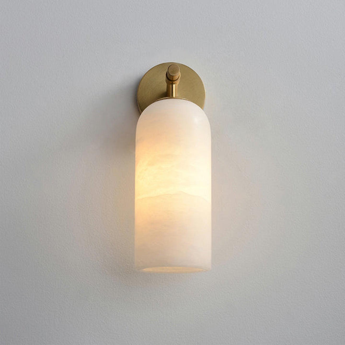 Clérachic Pillar wall light lit on grey, slim brass stem dropping to the glowing shade.