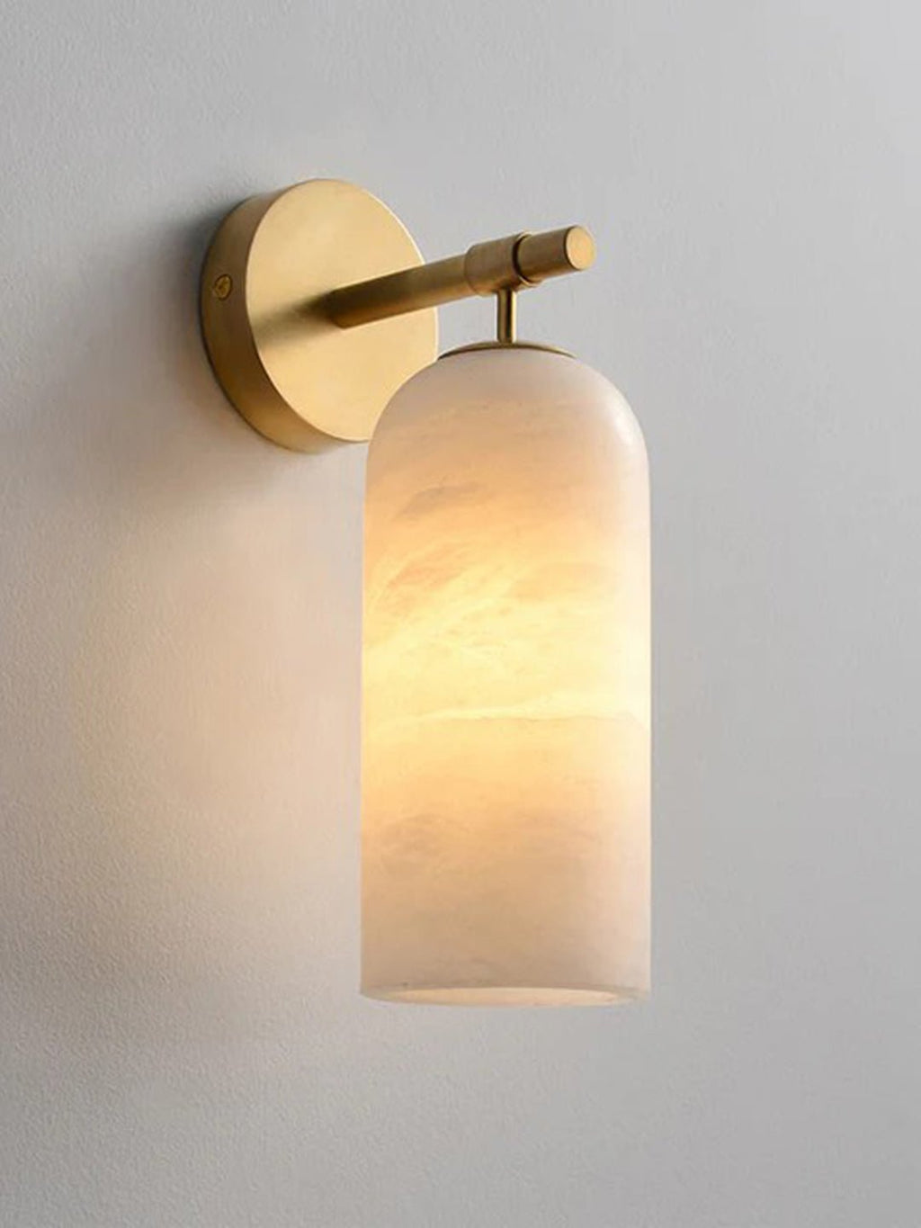 The Clérachic Pillar wall light lit on a pale wall, amber light banded across the alabaster.