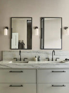 Clérachic Pillar wall lights set either side of two mirrors in a marble-topped bathroom.