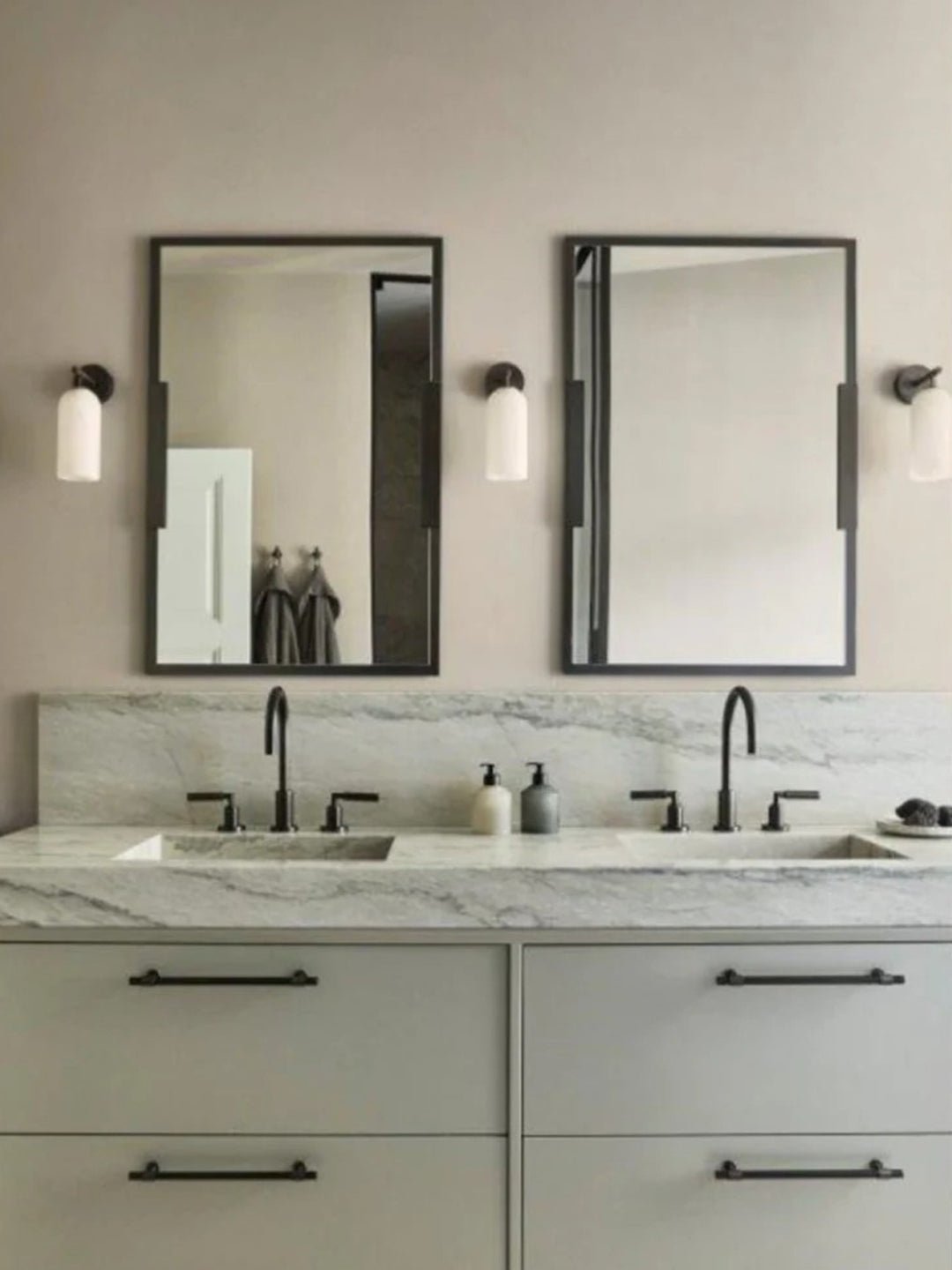 Clérachic Pillar wall lights set either side of two mirrors in a marble-topped bathroom.