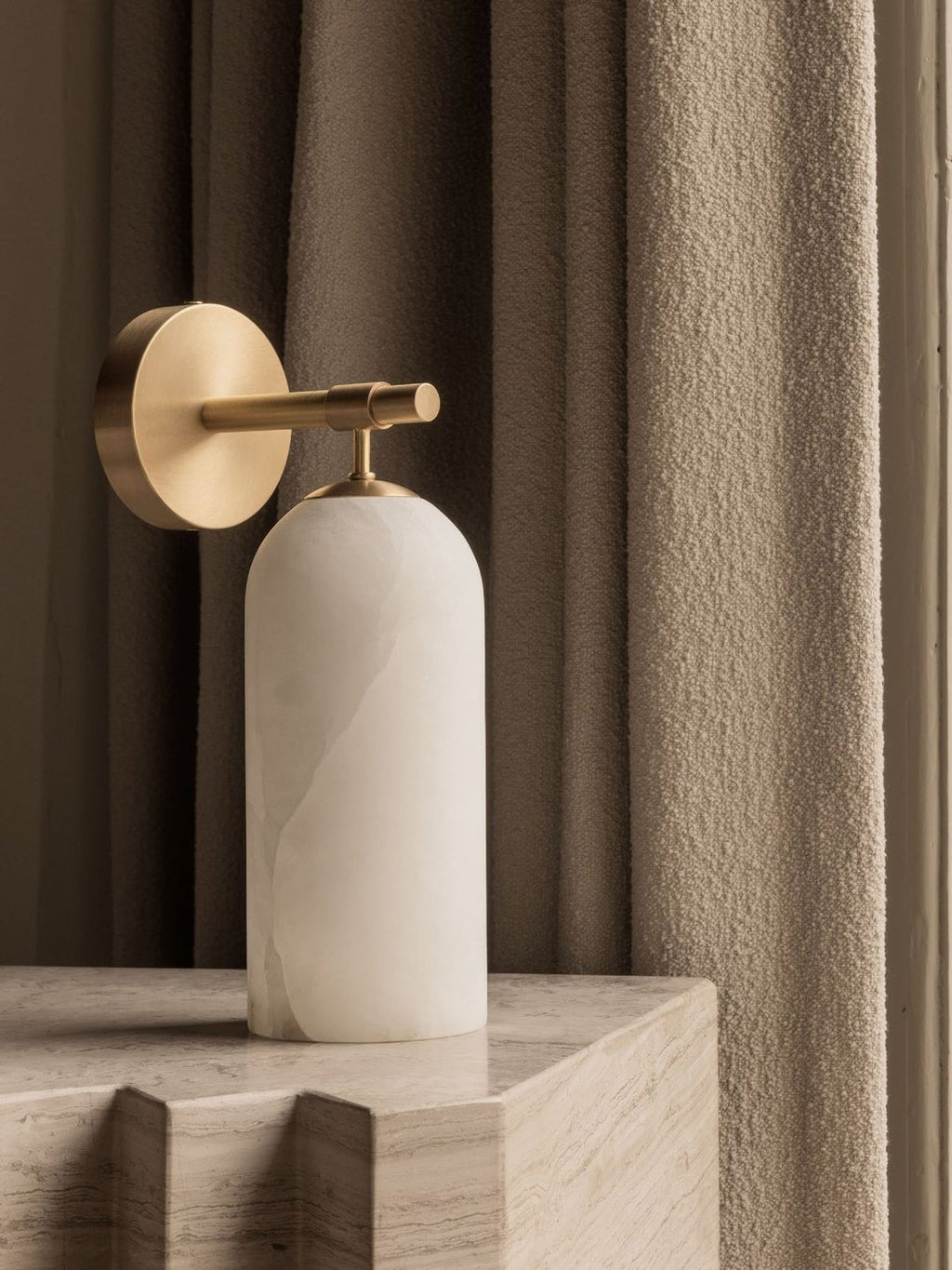 Clérachic Pillar wall light styled on a travertine block against a heavy woven curtain.