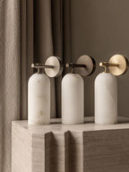 Three Clérachic Pillar wall lights lined up on a stone plinth in brass and bronze finishes.