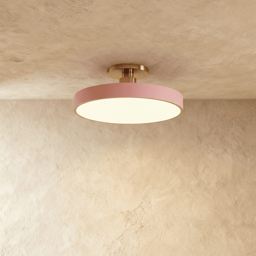 Clérachic ceiling light in dusty pink with a brass stem, its round drum glowing warm white against a plaster ceiling.