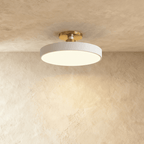 Clérachic ceiling light in white, its round drum diffuser glowing soft warm light beneath a brass ceiling stem.