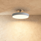 Clérachic ceiling light in grey, the flush-mount drum shade glowing warm white against a textured plaster wall.