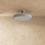Clérachic ceiling light in grey with a polished nickel stem, the round drum shade glowing warm white.