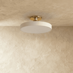 Clérachic ceiling light in white with a brass stem, the round drum shade glowing softly overhead.