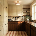 Clérachic ceiling light in pink glowing above a cream cabinetry kitchen with a terracotta checkerboard floor.