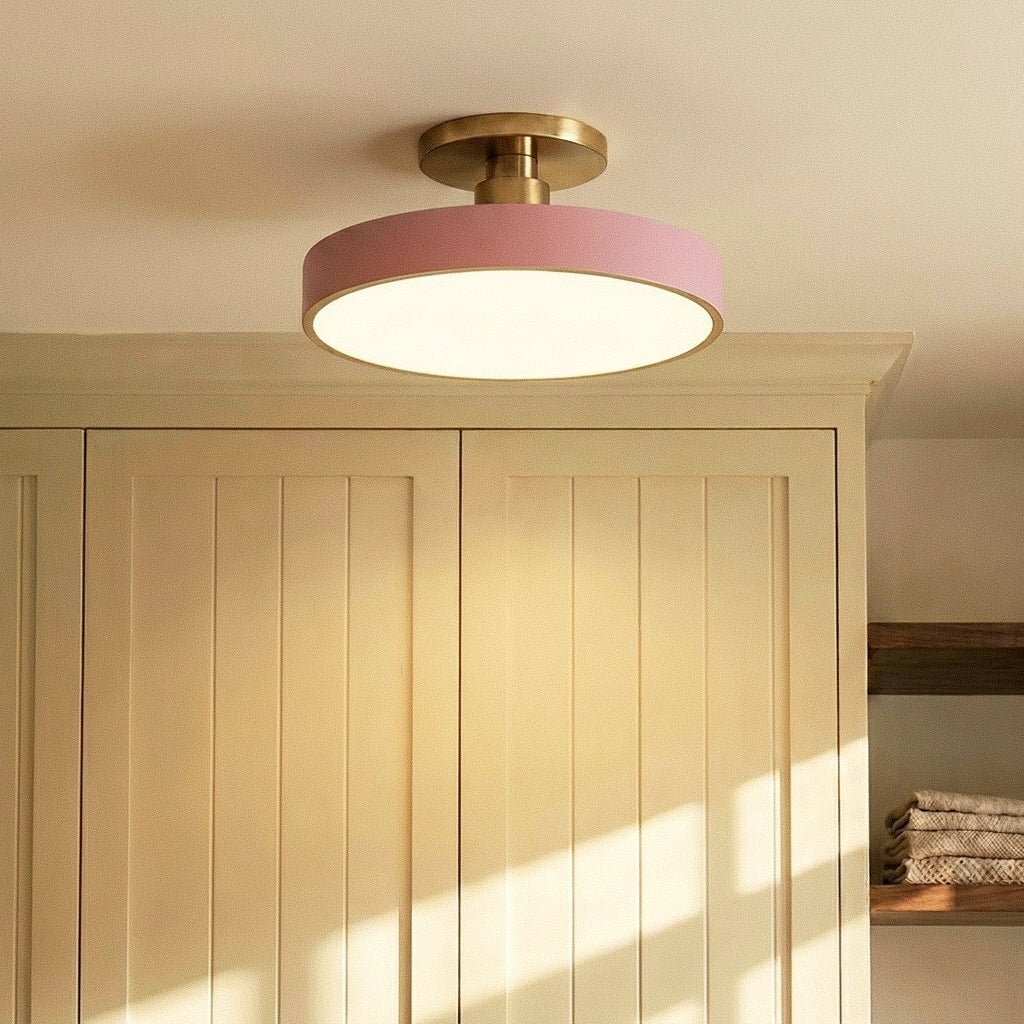 Clérachic ceiling light in pink mounted above a cream shaker cabinet, warm light falling across folded towels.