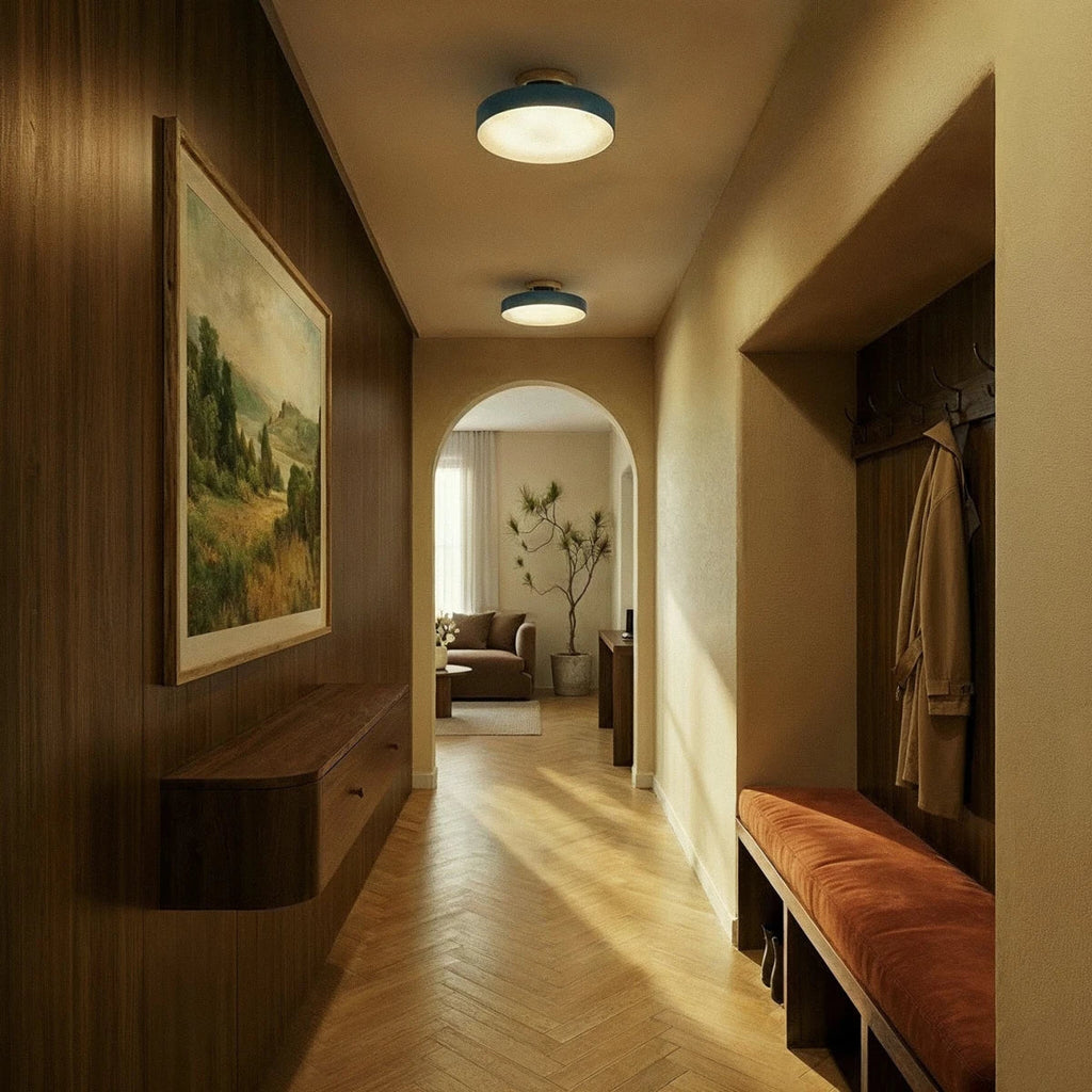 Two Clérachic ceiling lights in blue line a warm hallway, glowing above herringbone floors toward an arched doorway.