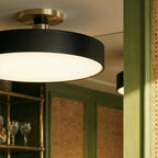 Close-up of a Clérachic ceiling light in matte black, its warm glow set against green wood-panelled cabinetry.