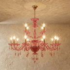 Clérachic pink crystal chandelier with brass candle arms and cascading crystal drops, shown against a limewash wall.