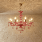 Clérachic pink crystal chandelier with eight brass candle arms and faceted crystal drops against a limewash wall.