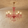 Clérachic pink crystal chandelier, six brass candle arms and crystal pendants, hung against a warm limewash wall.