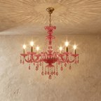 Clérachic pink crystal chandelier, six brass candle arms and crystal pendants, hung against a warm limewash wall.