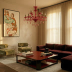 Clérachic pink crystal chandelier lights a living room with olive armchairs, a lacquered coffee table and sheer curtains.