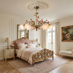 A Clérachic rose chandelier glowing above a carved gilt bed with a pink headboard, in a cream bedroom with a patterned rug.