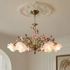 Close view of this Clérachic chandelier hanging from a decorative white ceiling rose, with lit frosted rose shades and ceramic flowers on gold branches.