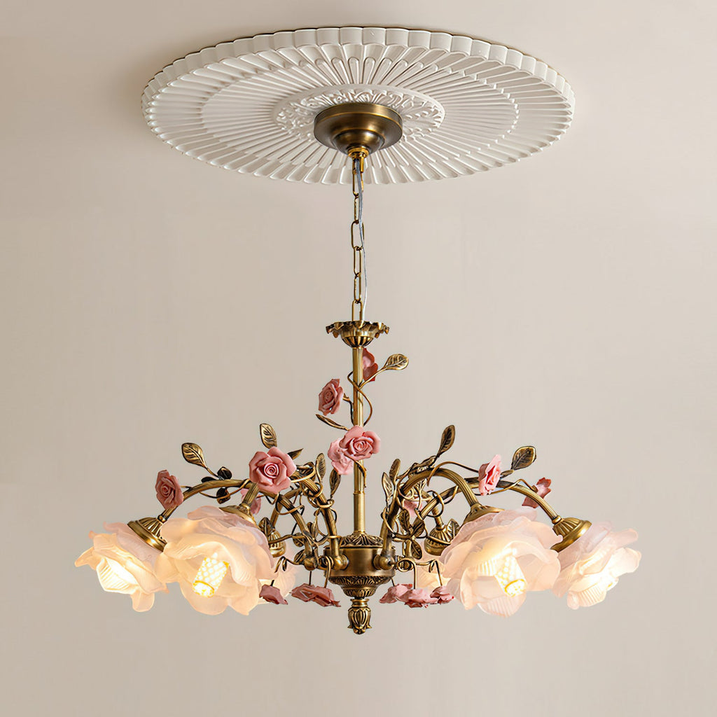 Clérachic chandelier lit beneath a round fluted ceiling rose on a pale wall, its antique gold chain and arms trailing small pink roses.