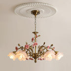 Clérachic chandelier lit beneath a round fluted ceiling rose on a pale wall, its antique gold chain and arms trailing small pink roses.