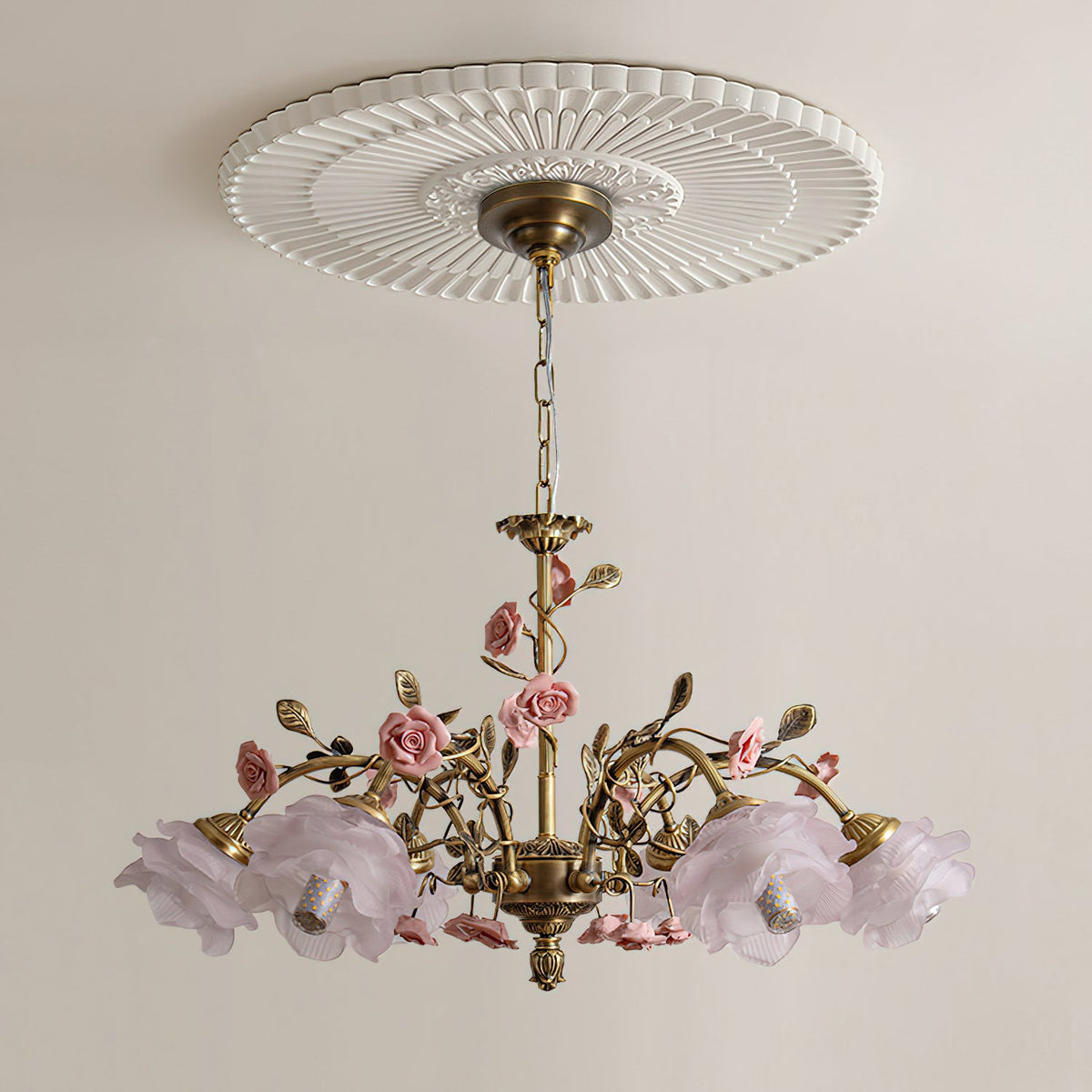 Clérachic chandelier with pale lilac glass rose shades, unlit, hanging from a white fluted ceiling rose on a soft cream wall.