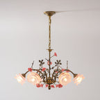 Clérachic chandelier lit against a pale grey wall, its gold chain leading to arms of leaves, pink ceramic roses and glowing glass blooms.