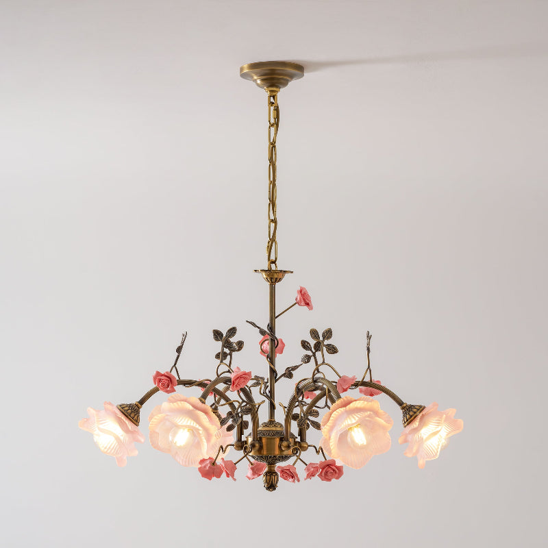 Clérachic chandelier lit against a pale grey wall, its gold chain leading to arms of leaves, pink ceramic roses and glowing glass blooms.