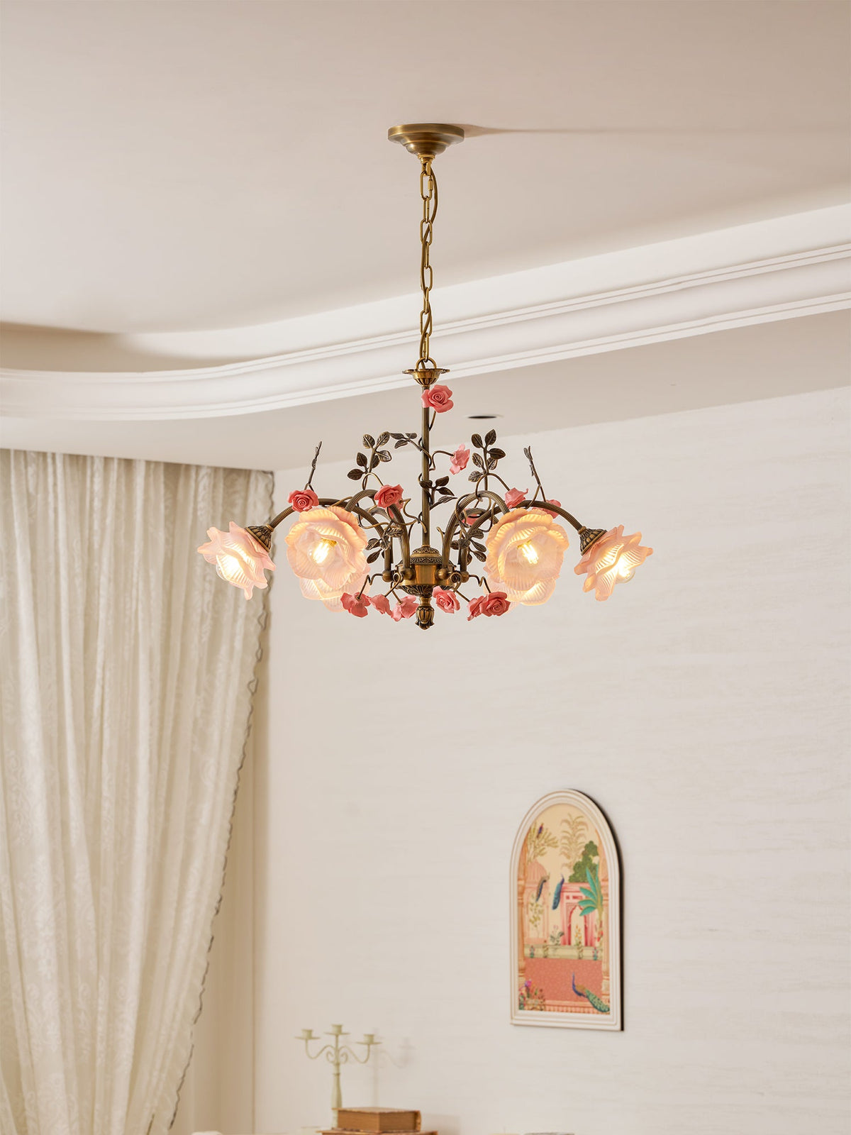 Clérachic chandelier lit in a cream room, hanging below a curved plaster ceiling with sheer curtains and an arched picture behind.